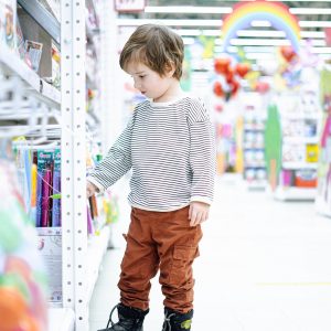 Cute toddler boy in striped shirt choosing toys at kids market